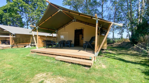 Safari tent with a wooden deck and outdoor seating at Camping de Tolbrug, surrounded by grass and trees.