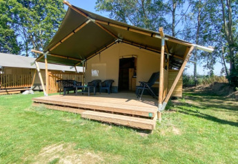 Safari tent with a wooden deck and outdoor seating at Camping de Tolbrug, surrounded by grass and trees.