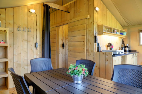 Vista interna di una tenda safari con pareti in legno, cucina e zona pranzo a Camping Dal van de Mosbeek, Paesi Bassi.