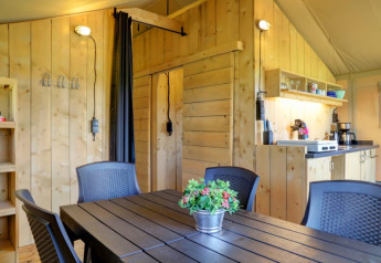 Interior view of a safari tent with wood-paneled walls, kitchen and dining area at Camping Dal van de Mosbeek, Netherlands.