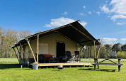 Tenda safari al Minicamping Falkenborg nei Paesi Bassi con veranda in legno e prato verde circostante.