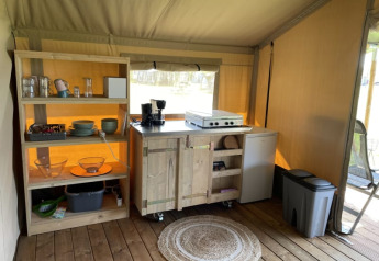 Kitchen area in Safari tent at Minicamping Falkenborg, Netherlands, with shelves, stove, and fridge.