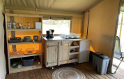 Angolo cucina nella tenda Safari al Minicamping Falkenborg, Paesi Bassi, con scaffali e fornello.