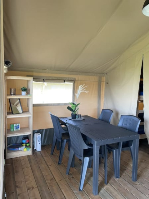 Interior de la tienda Safari en Minicamping Falkenborg, Países Bajos, con mesa, sillas y estantería.