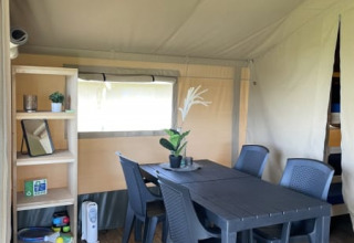 Interior de la tienda Safari en Minicamping Falkenborg, Países Bajos, con mesa, sillas y estantería.