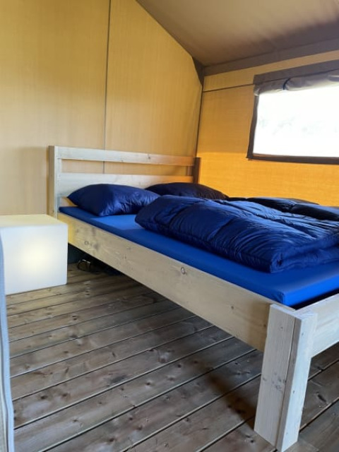 Cama de madera con ropa de cama azul en una tienda safari en Minicamping Falkenborg, Países Bajos.
