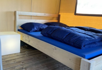 Cama de madera con ropa de cama azul en una tienda safari en Minicamping Falkenborg, Países Bajos.