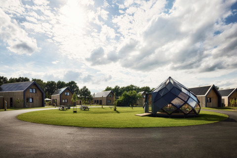 Vakantiepark Brinckerduyn in Friesland met moderne huisjes, glazen paviljoen en groene grasvelden onder bewolkte lucht.