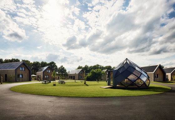 Vakantiepark Brinckerduyn in Friesland met moderne huisjes, glazen paviljoen en groene grasvelden onder bewolkte lucht.