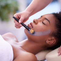 Una mujer recibe una mascarilla facial aplicada con brocha mientras se relaja, posiblemente en un spa de glamping.