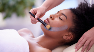 Een vrouw ontvangt een gezichtsmasker met een kwast terwijl ze ontspant, waarschijnlijk in een glampingresort.