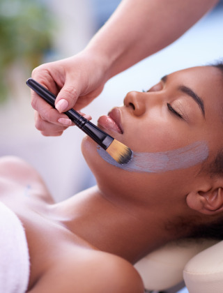 Una mujer recibe una mascarilla facial aplicada con brocha mientras se relaja, posiblemente en un spa de glamping.