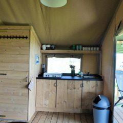 Interior de una tienda safari con cocina de madera y terraza en Minicamping de Vrolijke Flierefluiter.