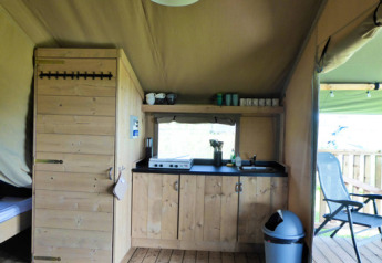 Interior of a safari tent with wooden kitchen, stove, and terrace at Minicamping de Vrolijke Flierefluiter.