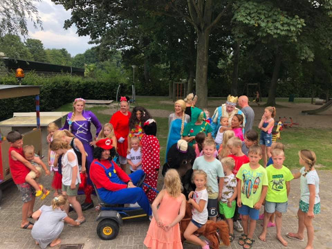 Groep kinderen en volwassenen in kleurrijke kostuums vieren feest in een vakantiepark in Zuid-Holland.