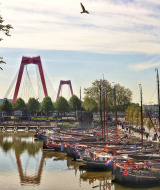 Barcos atracados en un canal tranquilo con un puente rojo icónico y edificaciones históricas en Róterdam.