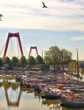 Boten aangemeerd in een rustige Rotterdamse haven met op de achtergrond de rode Willemsbrug en oud gebouw.
