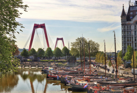 Barcos atracados en un canal tranquilo con un puente rojo icónico y edificaciones históricas en Róterdam.