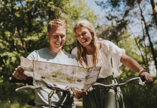 Twee mensen glimlachen terwijl ze samen een kaart lezen op hun fietsen in het bos bij Beerze Bulten.