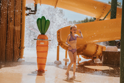 Een meisje speelt bij een waterglijbaan en een grote wortelwaterspuiter in Beerze Bulten vakantiepark.