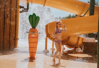 Een meisje speelt bij een waterglijbaan en een grote wortelwaterspuiter in Beerze Bulten vakantiepark.