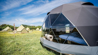 Cast Away Dome Nature House offers glamping in a geodome and tents on a grassy field under blue skies.