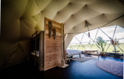 Vista interna di Cast Away Dome a TinyParks Cast Away, con letto, piante e grande finestra panoramica.