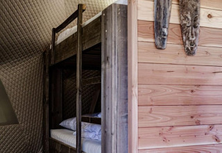 Binnenkant van een natuurhuisje met houten stapelbed, houten wanden en maskers in Cast Away Dome.