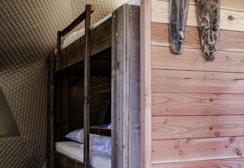 Interior de una casa natural con literas rústicas, paneles de madera y máscaras tribales en Cast Away Dome.