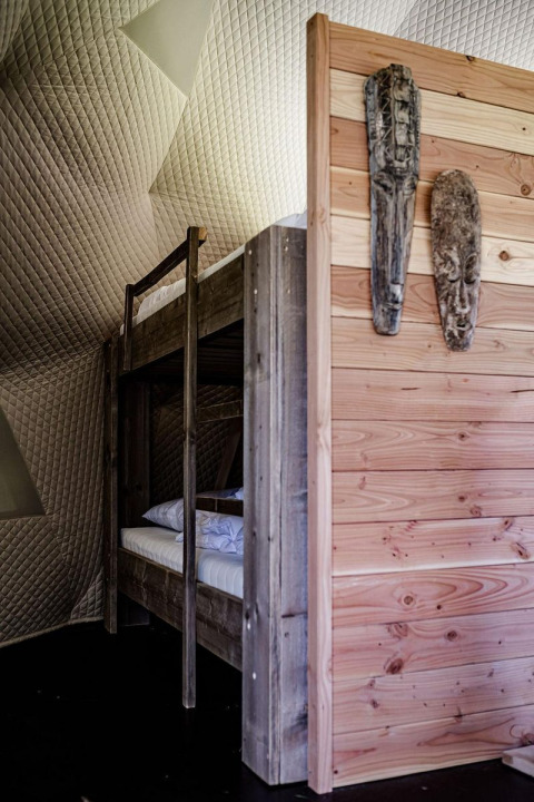 Binnenkant van een natuurhuisje met houten stapelbed, houten wanden en maskers in Cast Away Dome.