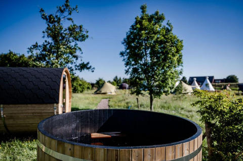 Sitio de glamping al aire libre con una tina caliente de madera, sauna y tiendas entre árboles y césped.