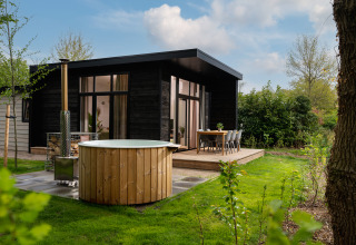 Moderne feriehytte med udendørs spabad, spisebord og grøn have ved Holiday Park Mölke i Overijssel, Holland.
