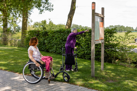 Zwei Frauen mit Gehhilfe und Rollstuhl erkunden CharmeCamping De Regge-Vallei in Overijssel, Niederlande.