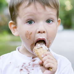 Kleine jongen met ijs op zijn gezicht eet een hoorntje op een vakantiepark met glampingverblijven.