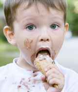 Niño pequeño con helado en la cara comiendo un cono en un parque vacacional con glamping al aire libre.