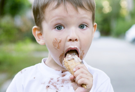 Jonge jongen met ijs op zijn gezicht eet een ijsje op een vakantiepark met glampingaccommodaties.