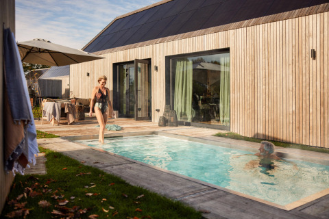 Frau im Badeanzug am Pool neben einem modernen Holzhaus im Ferienpark De Weelderik, Gelderland, Niederlande.