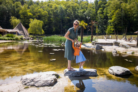 Madre e hija con gafas de sol disfrutan junto a un estanque en Cosy Cabins, parque de vacaciones en Limburg, Bélgica.