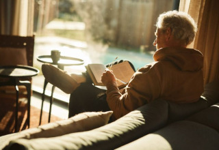 Older man relaxing and journaling on a sofa in sunlight at De Weelderik holiday park, Gelderland, Netherlands.