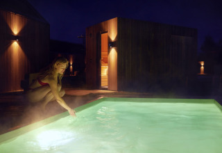 Donna in costume tocca una piscina illuminata di notte al parco vacanze De Weelderik in Gheldria, Olanda.
