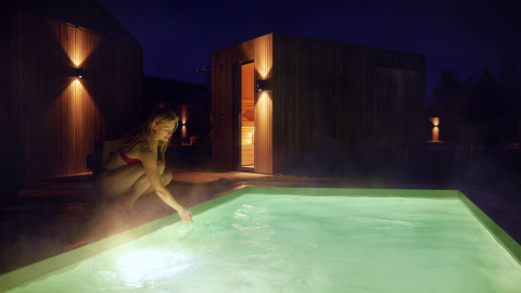 Mujer en traje de baño toca la piscina iluminada por la noche en De Weelderik, Gelderland, Países Bajos.