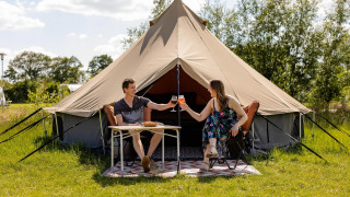Dos personas disfrutan de una comida frente a una tienda glamping en CharmeCamping De Regge-Vallei en los Países Bajos.