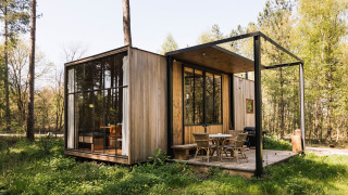 Moderne houten hut met grote ramen en terras, gelegen in een groene open plek in het bos in de lente.