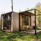 Moderne houten hut met grote ramen en terras, gelegen in een groene open plek in het bos in de lente.