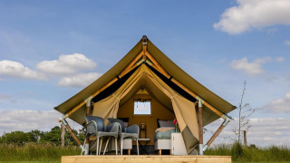 Tienda safari en CharmeCamping De Regge-Vallei, Países Bajos, con muebles modernos y cielo azul.