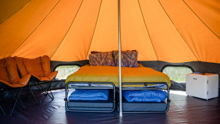 Interior de la Luxe belltent en CharmeCamping De Regge-Vallei, Países Bajos, con cama, sillas y mini nevera.