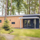 Moderne Forest Villa lodge ved Holiday park Ackersate i Holland, omgivet af frodige træer og grønt.