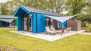 Cabaña de caza azul con sauna y terraza en Holiday Park Ackersate, Países Bajos, rodeada de árboles.