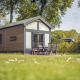 Lille sommerhus ved Holiday park Ackersate i Holland, omgivet af grønne områder og udendørs møbler.