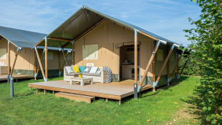 Tienda de glamping moderna con terraza amueblada al aire libre, rodeada de césped verde y naturaleza.
